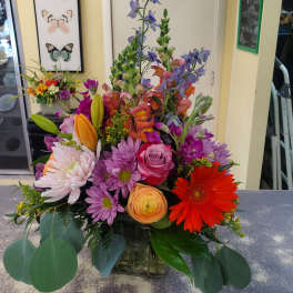 Mixed bouquet with roses, gerbera daisies, lilies, and purple blooms in a glass vase