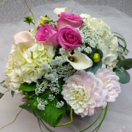 Pink roses and pale blooms arranged with white calla lilies in a bouquet