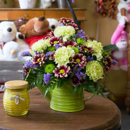 Mixed flower arrangement in a green metal container beside a yellow jar candle.