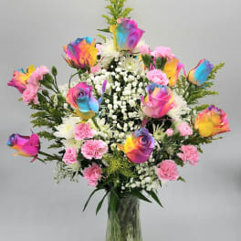Rainbow-colored roses and pink carnations in a glass vase