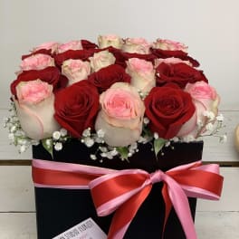 Red and blush roses arranged in a black box with a pink ribbon bow