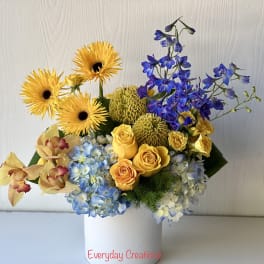 Bouquet of yellow gerbera daisies, blue hydrangeas, and yellow roses in a white vase