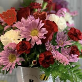 Mixed pink, red, and white flowers in a white "Bee Mine" container
