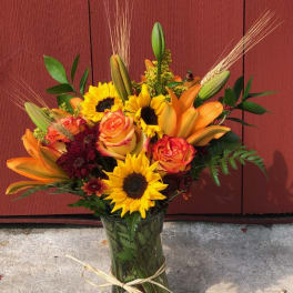 Bouquet of sunflowers, orange lilies, and roses in a glass vase
