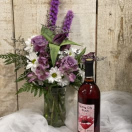Purple and white bouquet in a glass vase beside a bottle of wine