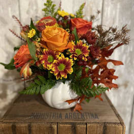 Autumn bouquet with orange roses and yellow-red chrysanthemums in a white pumpkin vase