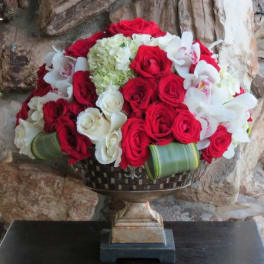 Red and white rose arrangement with white orchids in a decorative pedestal vase