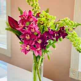 Pink and green orchids arranged in a tall clear vase