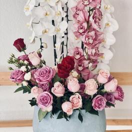 Pink and white orchids with roses in a round blue vase