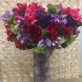 Tall bouquet of red, purple, and green flowers in a wrapped vase