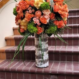 Large bouquet of orange and peach roses in a birch-style vase
