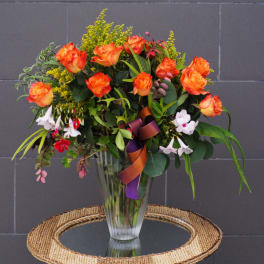 Orange roses in a clear glass vase with mixed greenery and small white flowers