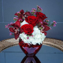Red roses, burgundy orchids, and white hydrangeas in a red glass vase