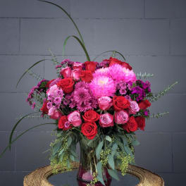 Bouquet of red and pink roses with magenta blooms in a glass vase