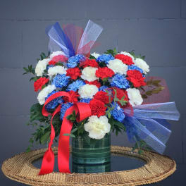 Bouquet of red, white, and blue carnations in a green vase with ribbon bows