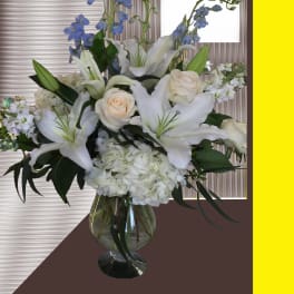 White lilies and roses arranged in a glass vase with blue flowers