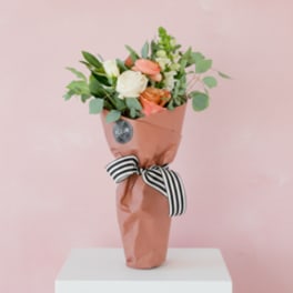 Wrapped bouquet of peach and white roses with greenery and a striped ribbon