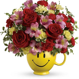 Bouquet of red roses, pink alstroemeria, and yellow carnations in a smiley-face mug