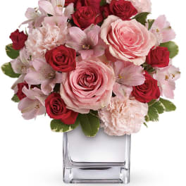Pink and red roses with pale pink flowers in a clear glass vase