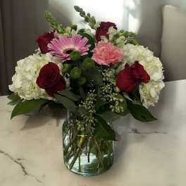 Bouquet of red roses, pink gerbera daisy, and white hydrangeas in a glass vase