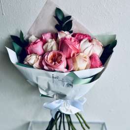 Bouquet of pink and cream roses wrapped in white paper with a ribbon