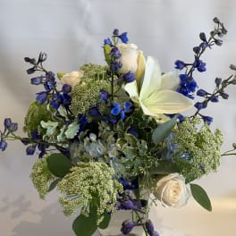 White roses and blue flowers in a clear glass vase