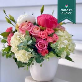 Pink and white roses, peonies, and hydrangeas arranged in a white ceramic pot