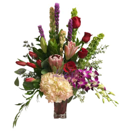 Mixed bouquet in a glass vase with red roses, pink lilies, and purple orchids