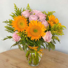 Pink roses and orange sunflowers arranged in a clear glass vase.