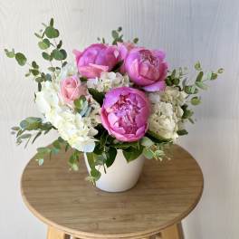 Pink peonies and roses arranged in a white pot