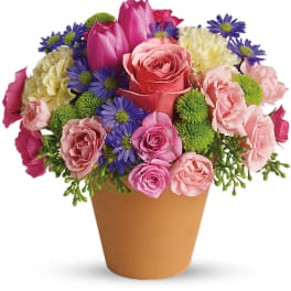 Mixed bouquet of pink, purple, and cream flowers in a tan pot