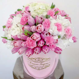 Round pink hatbox filled with pink tulips, pink carnations, and white hydrangeas.