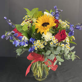 Bouquet of sunflowers, red roses, and blue flowers in a glass vase