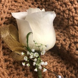 White rose boutonniere with gold ribbon on a brown textured background