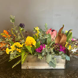 Mixed floral arrangement in a wooden box with yellow, pink, orange, and white blooms