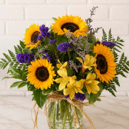 Bouquet of sunflowers and purple flowers in a glass vase with a raffia bow