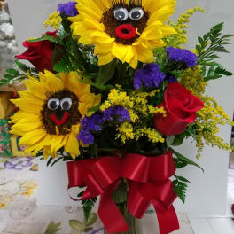 Bouquet with sunflowers, red roses, and a red ribbon in a glass vase