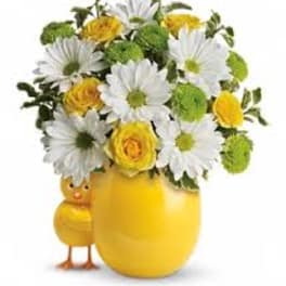 Yellow and white flower arrangement in a yellow vase with a chick figurine