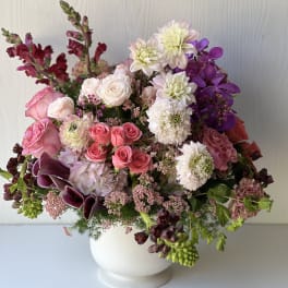 Mixed pink, white, and purple flowers arranged in a white vase