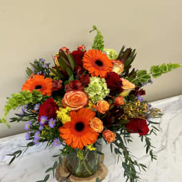 Bright mixed bouquet with orange gerbera daisies and red roses in a glass vase