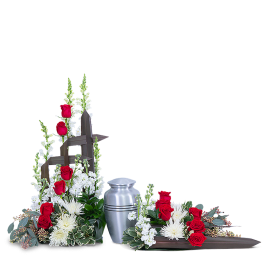 Red roses and white flowers arranged around a silver urn and wooden cross