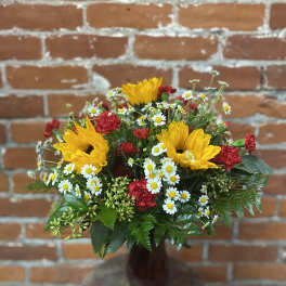 Bouquet of yellow sunflowers, red carnations, and white daisies in a brown vase