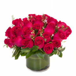Compact arrangement of hot pink roses in a low clear glass cylinder vase with a leaf-wrapped base