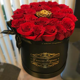 Red roses arranged in a black round box with a gold rose accent