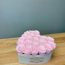 Pink roses arranged in a white heart-shaped box on a wooden table