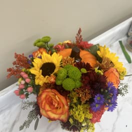 Colorful bouquet with sunflowers, roses, and chrysanthemums around a pumpkin