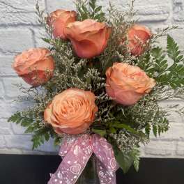 Peach roses in a glass vase with a pink ribbon