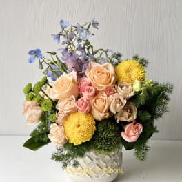 Peach and pink roses with yellow mums in a white vase