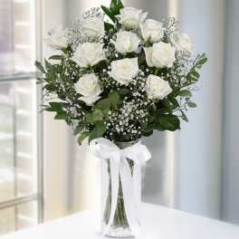 White roses arranged in a clear vase with a white ribbon.