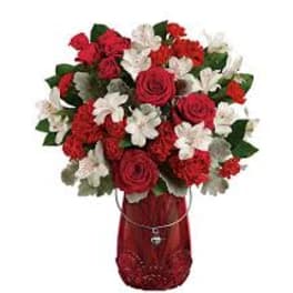 Red and white flower bouquet in a red vase with a heart charm